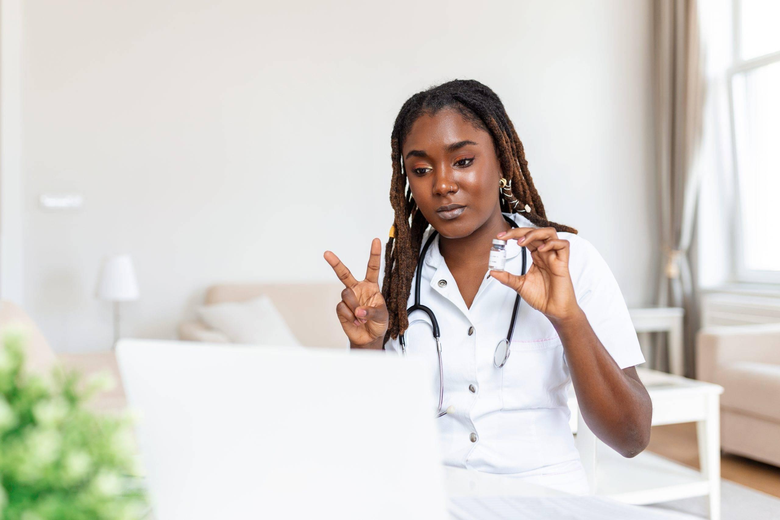 African oman doctor talking online with patient, making video call, looking at camera, young female wearing white uniform with stethoscope speaking, consulting and therapy concept